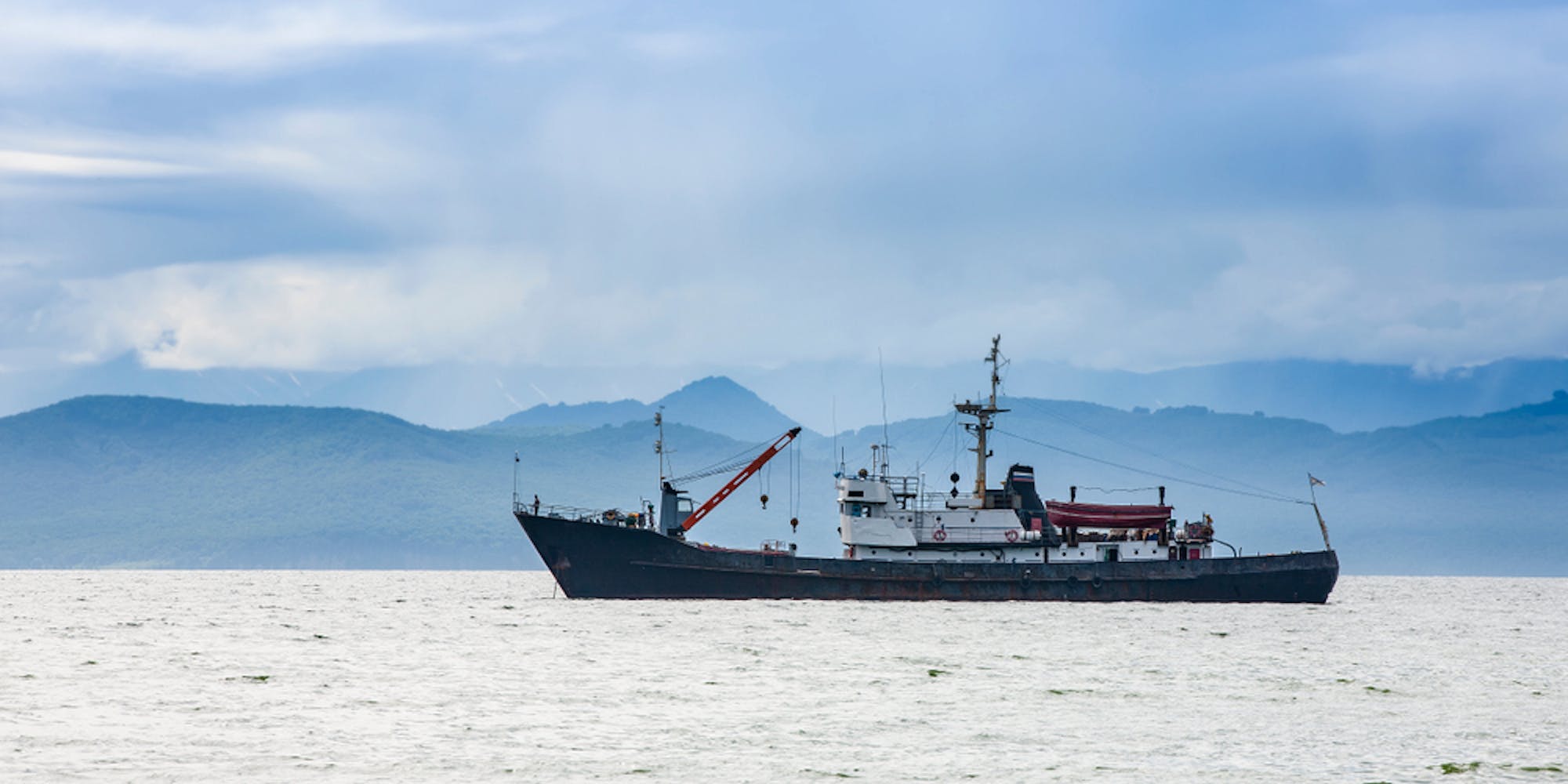 Large,Fishing,Vessel,On,The,Background,Of,Hills,And,Volcanoes